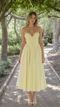 Front view of woman wearing yellow strapless corset midi dress in a park