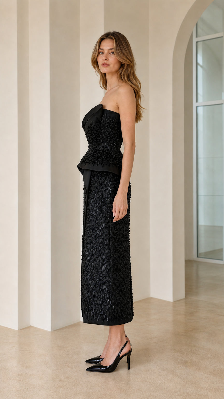 Side profile view of black strapless dress with peplum waist