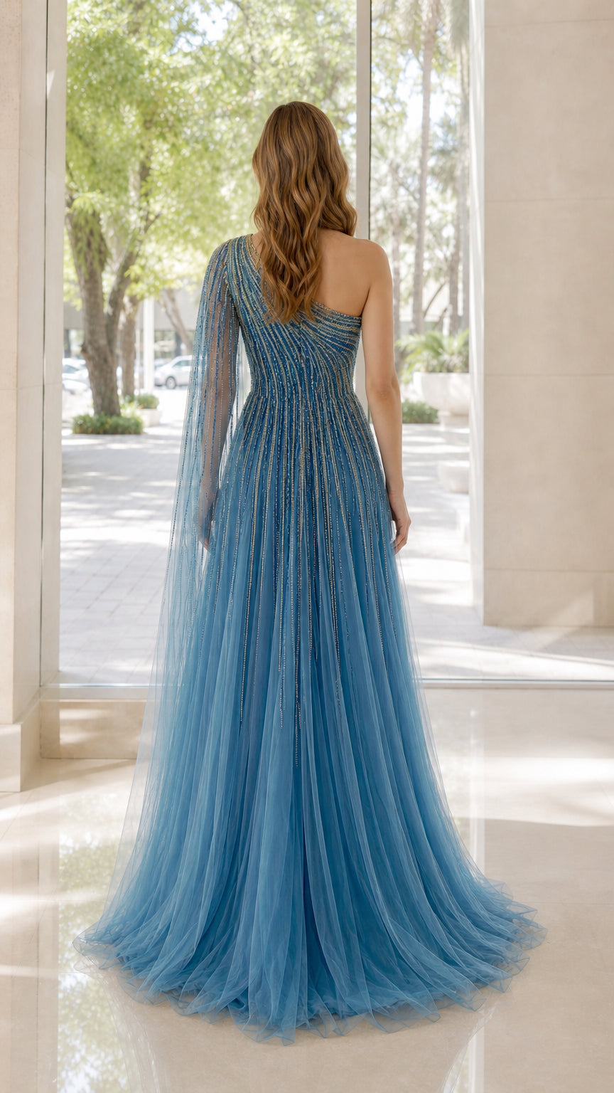 Back view of model wearing blue one-shoulder beaded dress with sweeping cape