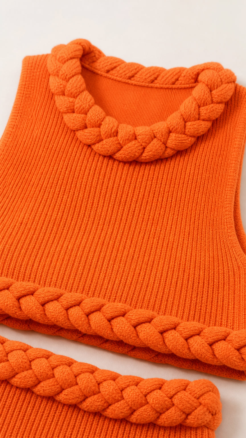 Close-up detail of textured knit fabric and braided trim on orange top and skirt