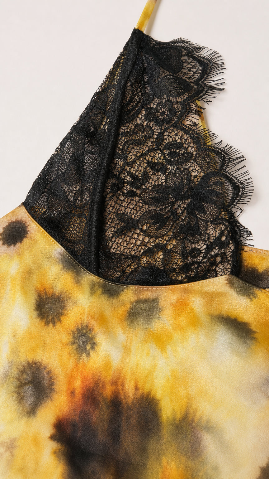 Close-up detail of black floral lace cup on yellow tie-dye fabric